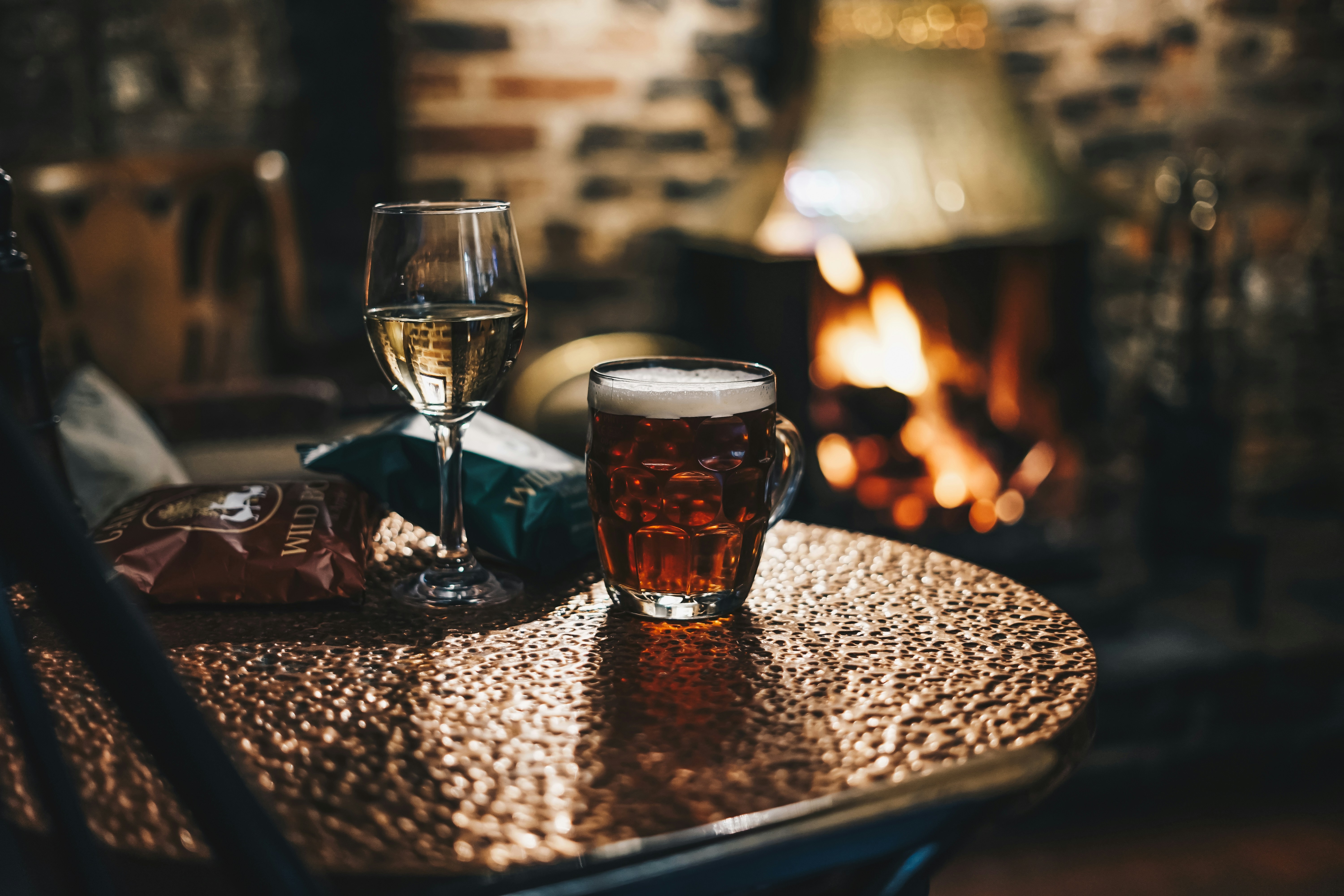 A pint of ale and a glass of white wine on a table beside a roaring fire inside a traditional Yorkshire pub